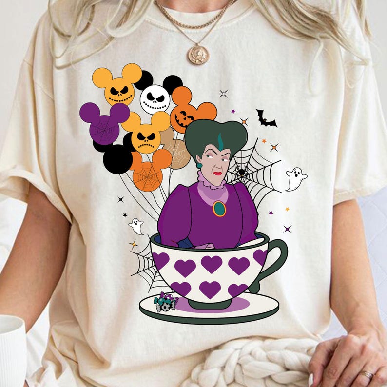 Pu&ograve; includere: T-shirt color crema con grafica a tema Halloween. Il design include un personaggio vestito di viola in una tazza da t&egrave; con motivi a cuore, circondato da palloncini a forma di Mickey Mouse, ragnatele, fantasmi e un pipistrello. Il tema generale &egrave; uno stile spettrale e da cartone animato.