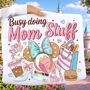 May include: White tote bag with the text "Busy doing Mom Stuff" in pink and brown. The bag features illustrations of a Minnie Mouse ear headband, high heel, shopping bag, and other mom-related items. Hearts and stars are scattered around the design.