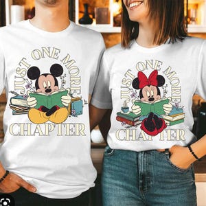 Op de afbeelding: Wit T-shirt met een afbeelding van Mickey Mouse die een boek leest. De tekst "Just One More Chapter" staat op het shirt gedrukt.