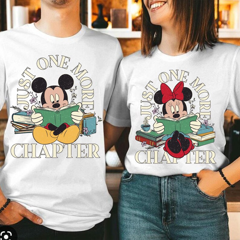 Op de afbeelding: Wit T-shirt met een afbeelding van Mickey Mouse die een boek leest. De tekst "Just One More Chapter" staat op het shirt gedrukt.