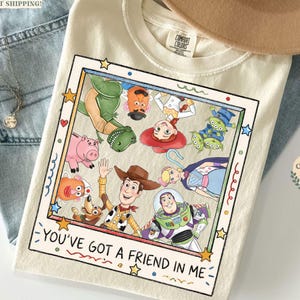 Puede incluir: Camiseta color crema con un gr&aacute;fico enmarcado de personajes de Toy Story. El gr&aacute;fico incluye a Woody, Buzz Lightyear, Rex y otros. El texto "YOU'VE GOT A FRIEND IN ME" est&aacute; en la parte inferior del marco.