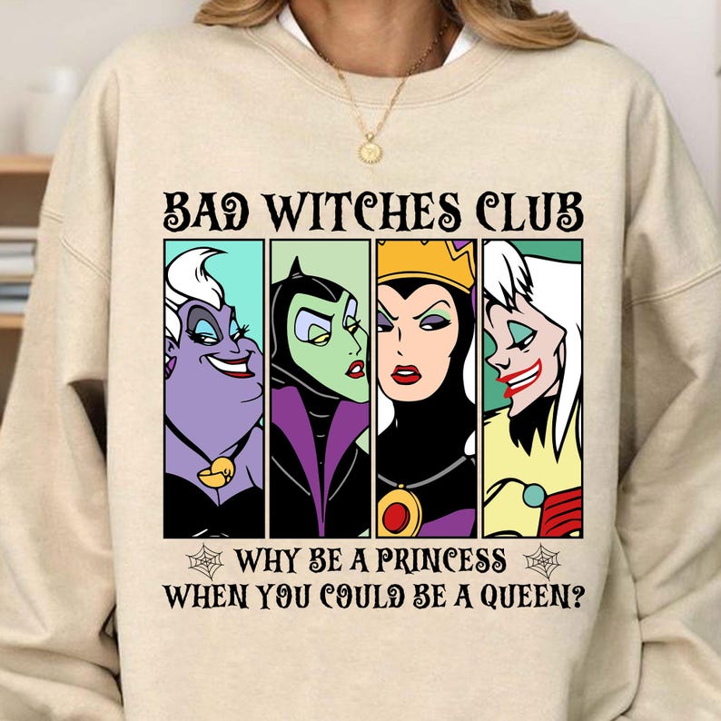 Puede incluir: Una sudadera beige con un estampado gr&aacute;fico de cuatro personajes de villanos de Disney, &Uacute;rsula, Mal&eacute;fica, la Reina Malvada y Cruella de Vil. El texto dice "Bad Witches Club" y "Why be a princess when you could be a queen?"