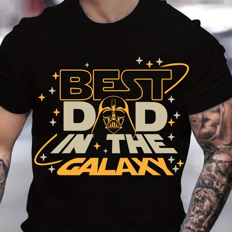 May include: Black t-shirt with a yellow and orange graphic that says "Best Dad in the Galaxy" with a Darth Vader silhouette in the middle.