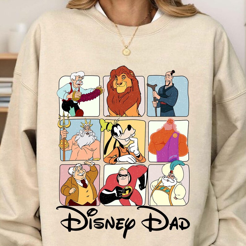 May include: A beige sweatshirt with a graphic print of various Disney characters in squares. The characters include Mickey Mouse, Donald Duck, Goofy, Simba, Aladdin, Hercules, and more. The text "Disney Dad" is printed below the graphic.