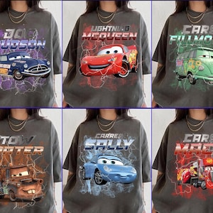 Può includere: Sei magliette grigie con grafiche dei personaggi del film Cars. Ogni maglietta mostra un personaggio diverso con il suo nome, tra cui Doc Hudson, Saetta McQueen e Cricchetto.