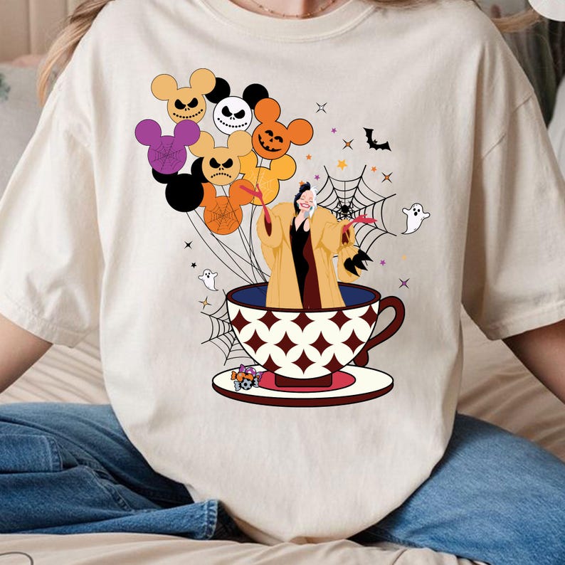 Pu&ograve; includere: T-shirt color crema con un design stravagante di Halloween. La grafica include un personaggio in una tazza da t&egrave;, circondato da palloncini a forma di teste di Topolino, ragnatele, fantasmi e pipistrelli. I palloncini sono di vari colori.