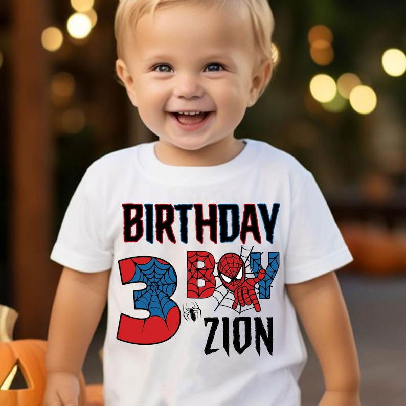 May include: White t-shirt with a red, blue, and black Spiderman graphic. The shirt says "Birthday Boy" and "3" with a spider web design. The name "Zion" is written below the number.