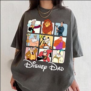 May include: A gray t-shirt with a graphic of nine Disney characters in squares. The characters include Mickey Mouse, Goofy, Simba, and more. The text "Disney Dad" is printed below the graphic.