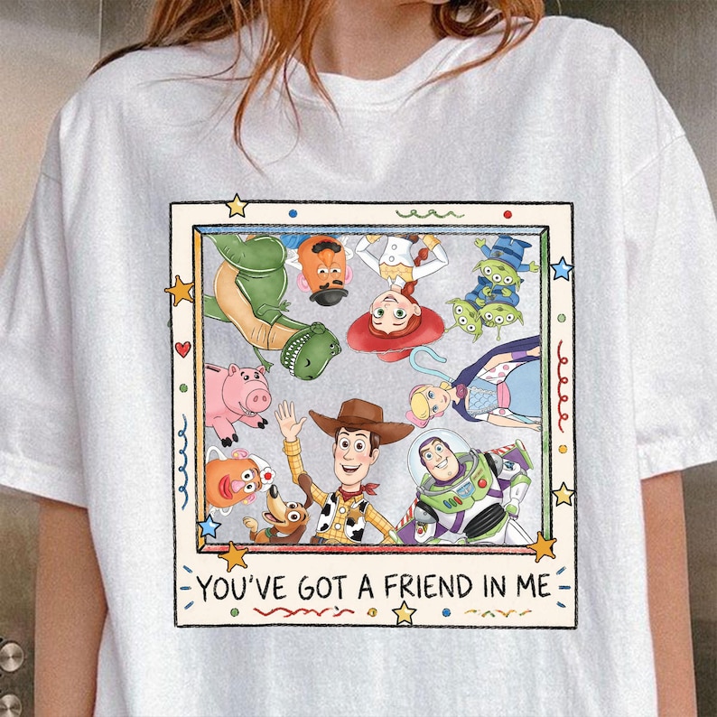 Puede incluir: Camiseta blanca con un gr&aacute;fico colorido de personajes de Toy Story. El dise&ntilde;o incluye a Woody, Buzz Lightyear y otros personajes, con el texto "YOU'VE GOT A FRIEND IN ME" en la parte inferior.