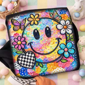 以下が含まれることがあります： カラフルなスマイリーフェイスのデザイン、花、蝶、市松模様のハートが特徴の黒いトートバッグ。アートワークは、色の虹で活気に満ちた質感のある外観をしています。イースターをテーマにした装飾が周りにあります。