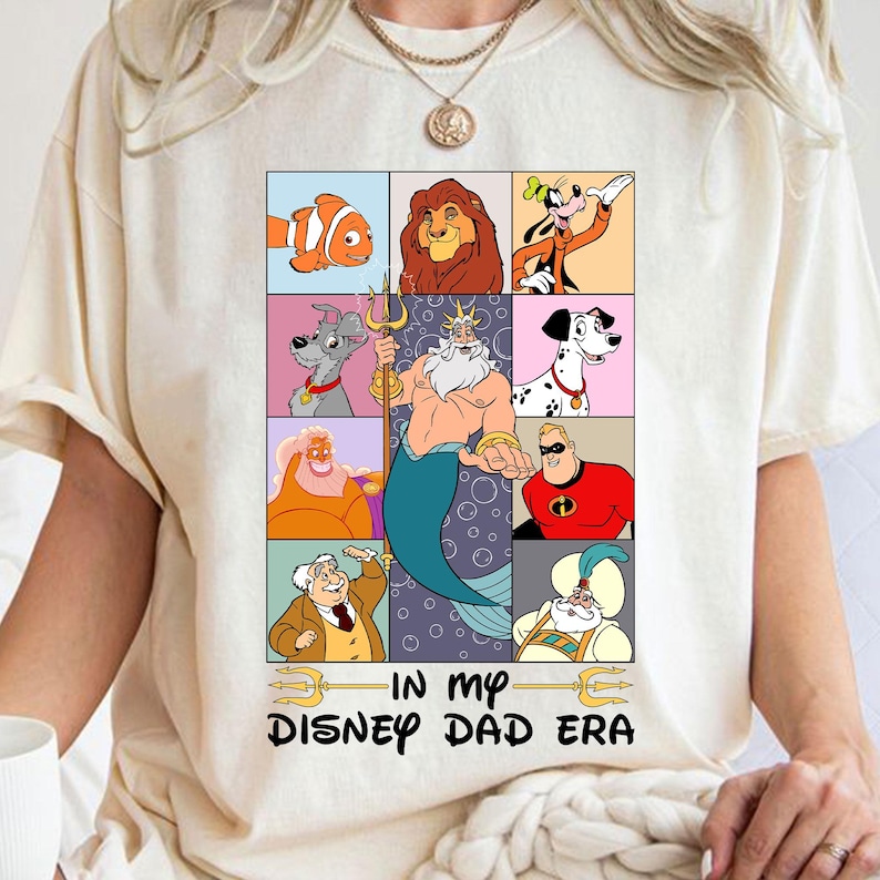 May include: A white t-shirt with a graphic of various Disney characters in a grid pattern. The characters include Ariel, Nemo,  Goofy,  and more. The text "In My Disney Dad Era" is printed below the graphic.