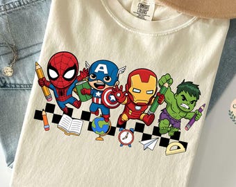 May include: Cream-colored t-shirt featuring a cartoon design of Spider-Man, Captain America, Iron Man, and the Hulk. The characters are depicted with school supplies on a black and white checkered pattern. The shirt is made of a soft, comfortable material.