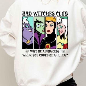Puede incluir: Sudadera blanca con un estampado gr&aacute;fico de cuatro villanas de Disney, &Uacute;rsula, Mal&eacute;fica, la Reina Malvada y Cruella de Vil. El texto dice "Bad Witches Club" y "Why be a princess when you could be a queen?"