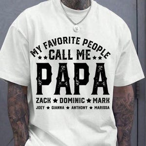 May include: White t-shirt with black text that reads "My Favourite People Call Me Papa" with names listed below.