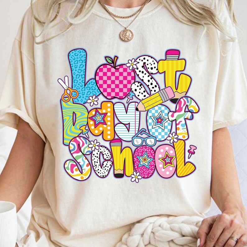 Może przedstawiać: Biały T-shirt z kolorową grafiką, na kt&oacute;rej widnieje napis "Ostatni dzień szkoły". Grafika składa się z r&oacute;żnych kształt&oacute;w i wzor&oacute;w, w tym gwiazd, kropek i wzor&oacute;w w kratkę.