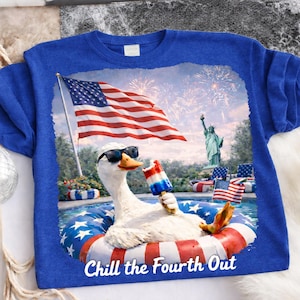 Könnte beinhalten: Blaues T-Shirt mit einem patriotischen Design. Es zeigt eine Gans mit Sonnenbrille, die in einem Pool mit einem aufblasbaren Ring schwimmt und ein rot-weiß-blaues Eis am Stiel hält. Die amerikanische Flagge und Feuerwerk sind im Hintergrund. Der Text lautet "Chill the Fourth Out."