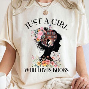 May include: A white t-shirt with the text "Just a girl who loves books" printed on it. The design features a silhouette of a woman with a bookshelf in her head, surrounded by flowers and butterflies.