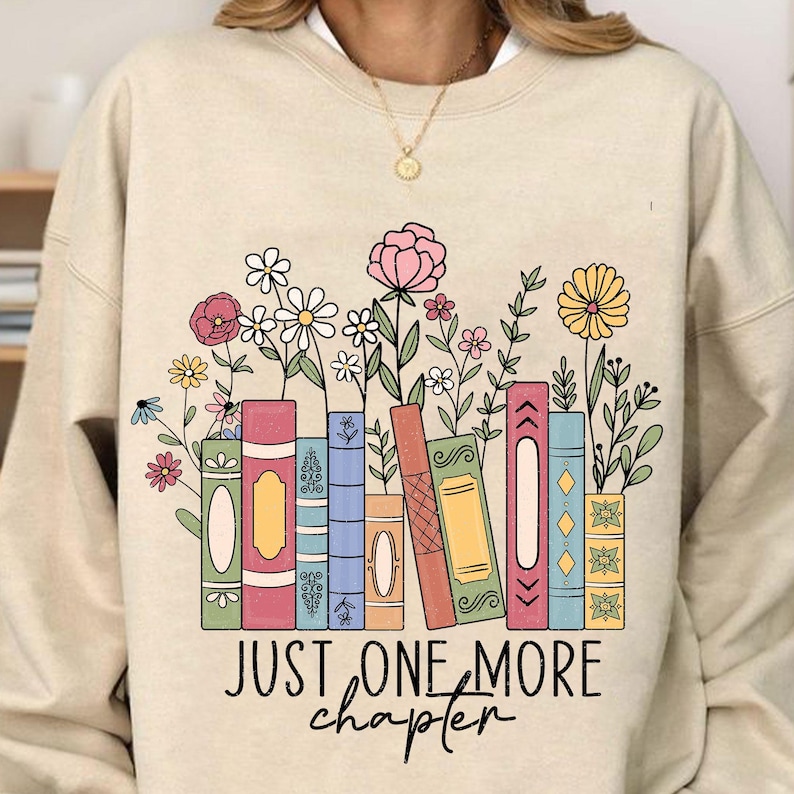 May include: Beige sweatshirt with a graphic of colorful books and flowers. The text "Just one more chapter" is printed below the graphic.