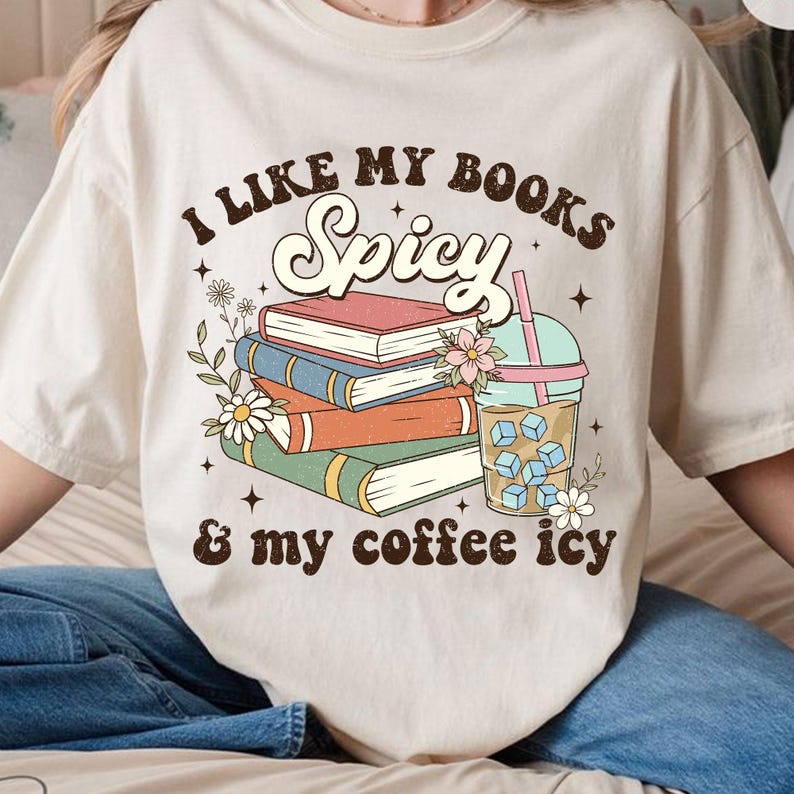 May include: A beige t-shirt with the text "I like my books spicy & my coffee icy" in brown lettering. The text is surrounded by a stack of books, a cup of iced coffee, and floral illustrations.