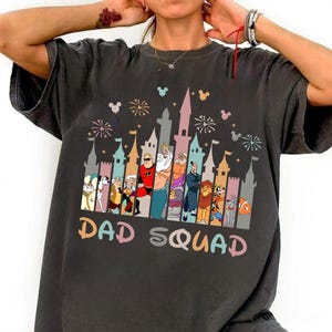 May include: A dark gray t-shirt with a graphic of a Disney castle and characters. The text "DAD SQUAD" is printed below the graphic.