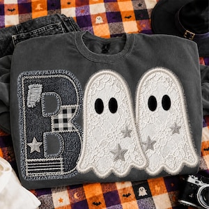 May include: A charcoal gray crewneck sweatshirt featuring a large letter B patch made of dark denim, black and white plaid, and stitched fabric. Next to the letter are two white lace ghost appliqués with black felt eyes and silver star accents.