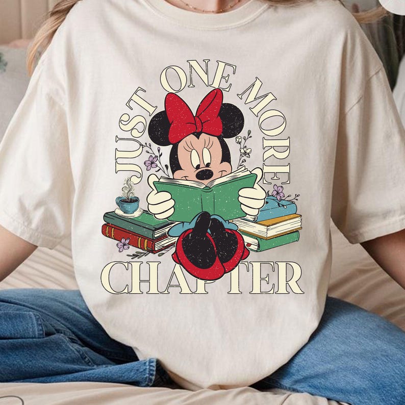 Op de afbeelding: Een wit T-shirt met een vintage-stijl afbeelding van Minnie Mouse die een boek leest. De tekst "Just One More Chapter" is in een cirkel rond Minnie Mouse gedrukt.