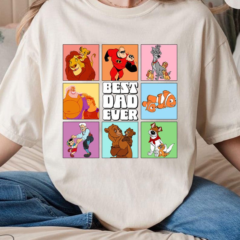 May include: White t-shirt with a colorful graphic of Disney characters. The graphic features a grid of nine squares with different Disney dads and their children. The text "BEST DAD EVER" is in the center of the graphic.