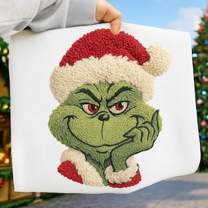 Könnte beinhalten: Ein grüner Grinch-Charakter mit rotem und weißem Weihnachtsmannhut und -kragen. Der Grinch lächelt und stützt sein Kinn auf seine Hand. Das Bild befindet sich auf weißem Hintergrund, mit einem Weihnachtsbaum im Hintergrund.