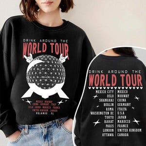 May include: Black sweatshirt with the text "DRINK AROUND THE WORLD TOUR" in red. The front features a geometric globe design and a list of cities. The back of the sweatshirt also has the text "DRINK AROUND THE WORLD TOUR" and a list of cities.