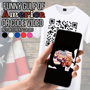 May include: A white t-shirt with a QR code printed on the front. The QR code is being scanned by a smartphone. The phone screen shows a graphic of a person with a red lip print on their face. The graphic says "The Gulf of America". The t-shirt is available in five different colours: black, white, blue, red, and pink.