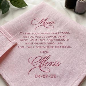 May include: A pink handkerchief with embroidered text. The text includes the word "Mom", a message, the name "Alexis", and the date "04-09-28". The handkerchief is made of a soft fabric.