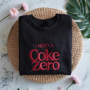 May include: Black sweatshirt with red embroidered text that reads "I need a Coke Zero".