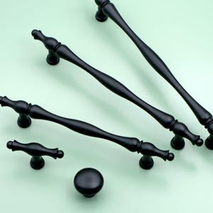 Peut inclure: Quatre boutons et poignées de cabinet noirs de différentes tailles et styles. Les boutons et les poignées ont une finition lisse et polie.