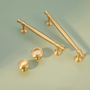 Può includere: Quattro tiretti per mobili in tinta oro. Due sono tiretti lunghi e dritti con un'estremità arrotondata. Due sono pomelli rotondi con un design circolare in rilievo.