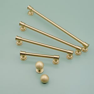 Op de afbeelding: Een set van vijf gouden kastgrepen in verschillende maten, met twee bijpassende ronde knoppen. De grepen zijn allemaal recht en hebben een eenvoudig, modern ontwerp.