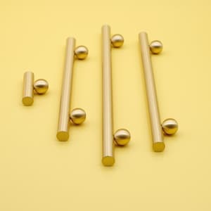 May include: Four gold-toned cabinet pulls with round knobs. The pulls are of different lengths.