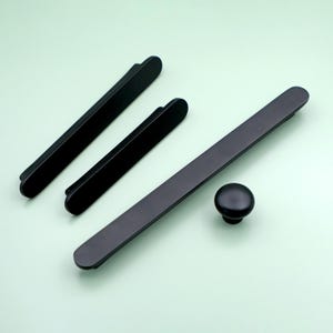 May include: A set of four black cabinet hardware pulls. The set includes three rectangular pulls and one round knob.