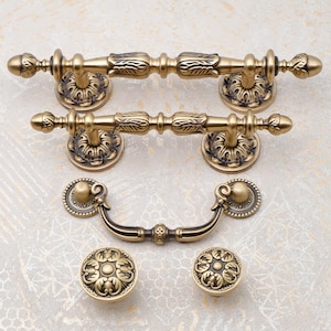 May include: A selection of antique brass cabinet hardware, comprising two long handles, a pull handle, and two round knobs. The hardware showcases intricate floral and leaf patterns, with a vintage appearance.