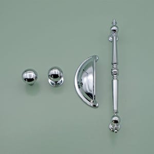 May include: A set of three chrome cabinet hardware pulls. The set includes a round knob, a cup pull, and a long bar pull.