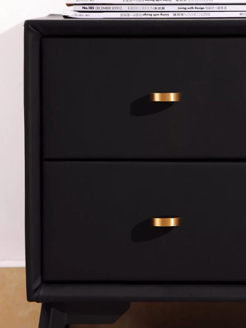 Pu&ograve; includere: Comodino nero a due cassetti con maniglie dei cassetti in metallo dorato. Il comodino ha un design semplice e moderno.