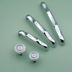 May include: Three silver cabinet pulls with a wavy design and two silver knobs with a floral design.