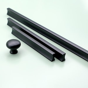 Peut inclure: Trois poignées de tiroir noires de forme rectangulaire aux bords arrondis. Un bouton noir rond est également inclus.