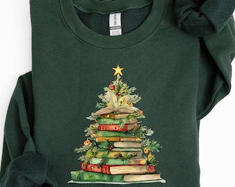 May include: A dark green sweatshirt featuring a Christmas tree design made of stacked books. The tree is decorated with greenery, ornaments, and a gold star on top. The sweatshirt is a crew neck style.
