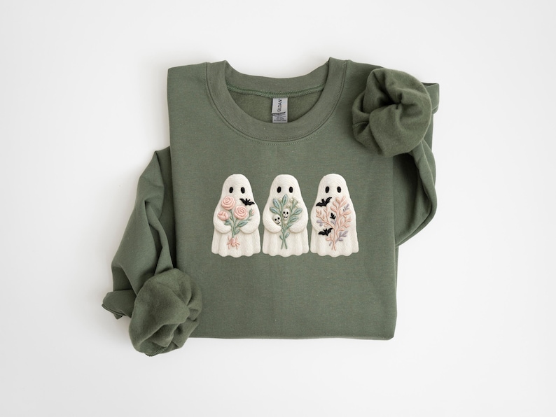 K&ouml;nnte beinhalten: Olivgr&uuml;nes Sweatshirt mit drei wei&szlig;en Geisterfiguren, die Blumen und Flederm&auml;use halten. Ein lang&auml;rmliges Oberteil f&uuml;r Halloween oder den Herbst. Das Design ist ein charmanter, saisonaler Stil.