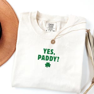 Pode incluir: Uma caneca de cerâmica branca com uma alça preta e o texto "But First, Coffee" em negrito preto. A caneca está sobre um fundo desfocado. A caneca tem aproximadamente 10 cm de altura.