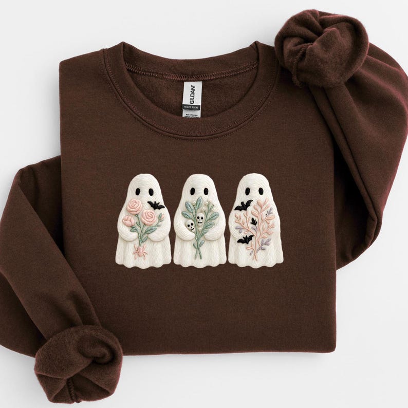 K&ouml;nnte beinhalten: Ein dunkelbraunes Sweatshirt mit drei wei&szlig;en Geisterfiguren, die auf der Vorderseite gestickt sind. Jeder Geist h&auml;lt einen anderen Strau&szlig; aus Blumen, Totenk&ouml;pfen und Flederm&auml;usen. Das Sweatshirt hat einen Rundhalsausschnitt und lange &Auml;rmel.