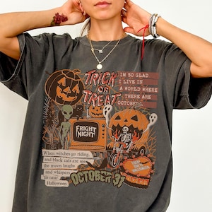 May include: Dark gray t-shirt with a Halloween-themed graphic. The design includes a jack-o'-lantern, an alien, a cat, and the words "Trick or Treat" and "Fright Night." Additional text includes "October 31" and a Halloween poem.