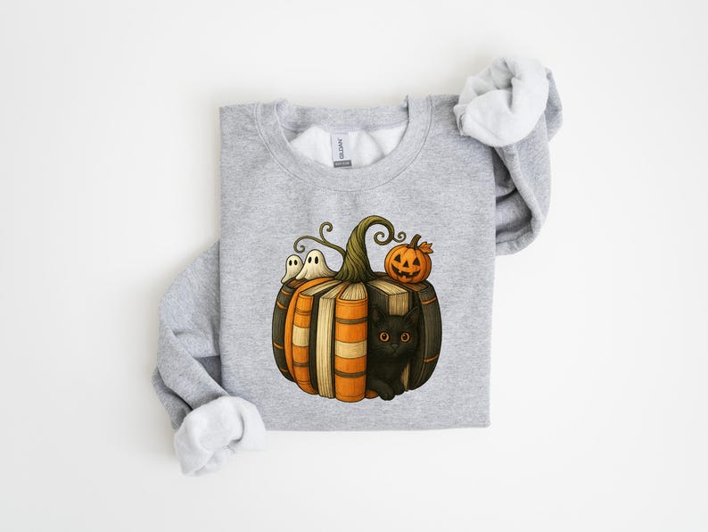 May include: A light gray sweatshirt featuring a Halloween-themed graphic. The design includes a pumpkin made of books, a black cat, two ghosts, and a jack-o'-lantern. The sweatshirt has a crew neck and long sleeves.