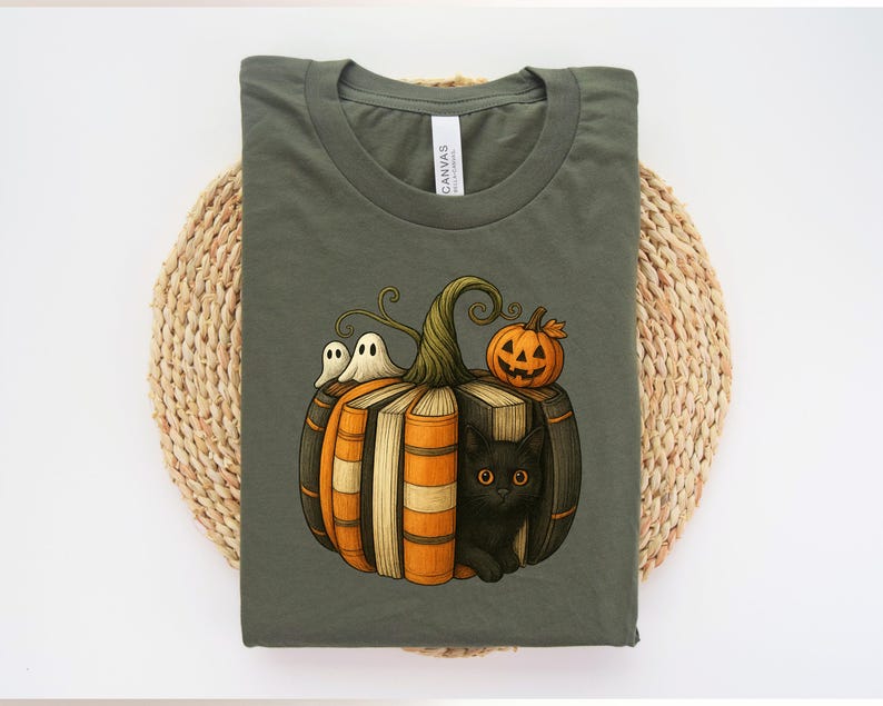 May include: Olive green t-shirt featuring a Halloween-themed graphic. The design includes a pumpkin made of books, with a black cat, two ghosts, and a jack-o'-lantern. The shirt is made of a soft material.