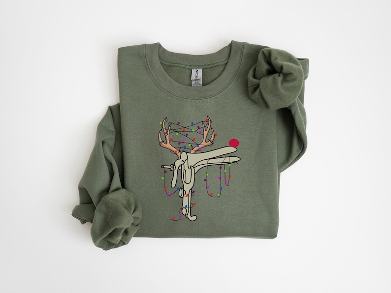 May include: A green sweatshirt with a white cartoon reindeer tangled in Christmas lights. The reindeer has red antlers and a red nose. The lights are multi-colored.